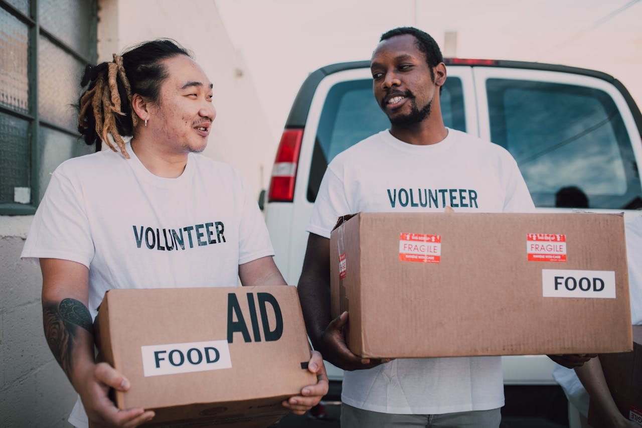 Two volunteers distributing food aid boxes for community relief outdoors.