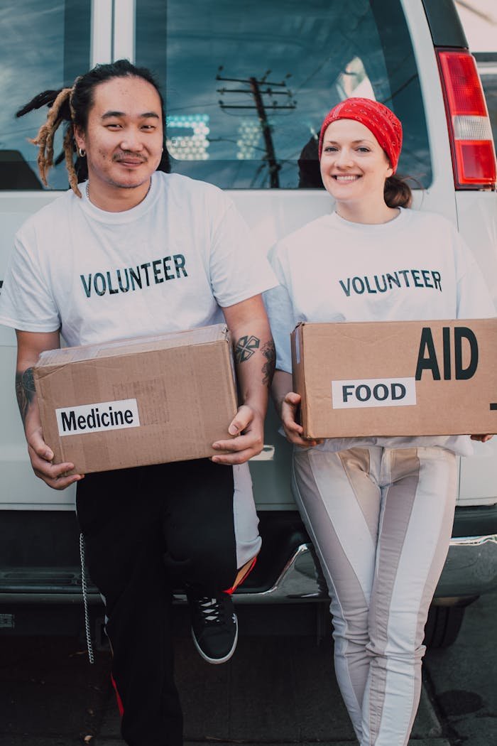 Two volunteers holding aid boxes with medicine and food labels, supporting charity causes.