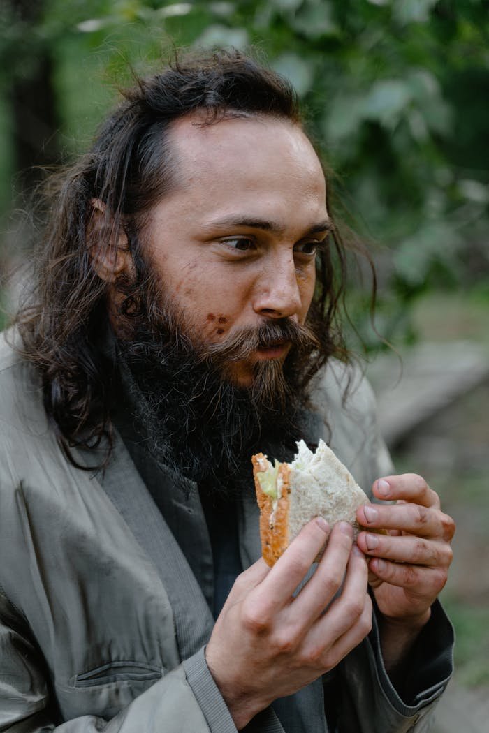 Bearded man in a gray jacket enjoying bread in an outdoor setting.